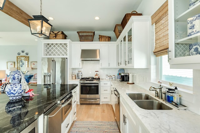 kitchen featuring stainless steel appliances, a sink, exhaust hood, white cabinetry, and decorative backsplash