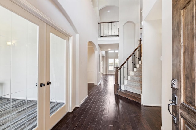 entrance foyer featuring wood-type flooring, a high ceiling, arched walkways, baseboards, and stairs