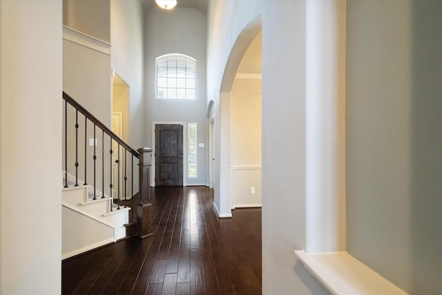 foyer entrance featuring dark wood-style flooring, arched walkways, a high ceiling, baseboards, and stairs