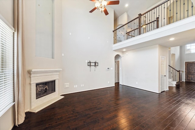 unfurnished living room featuring a premium fireplace, wood-type flooring, arched walkways, and a towering ceiling