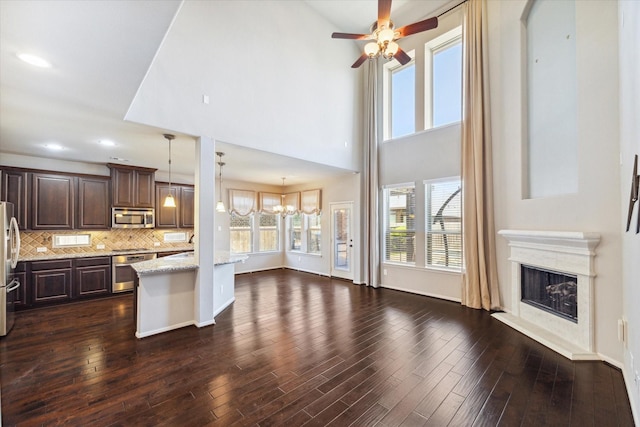 kitchen featuring tasteful backsplash, dark brown cabinetry, light stone counters, stainless steel appliances, and dark wood-style flooring