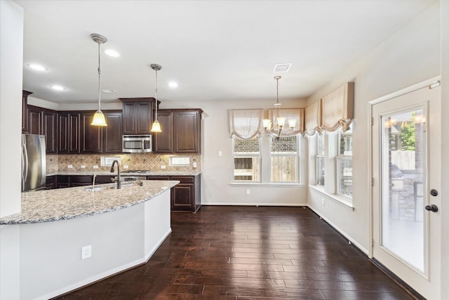 kitchen with a sink, light stone counters, backsplash, dark brown cabinetry, and appliances with stainless steel finishes