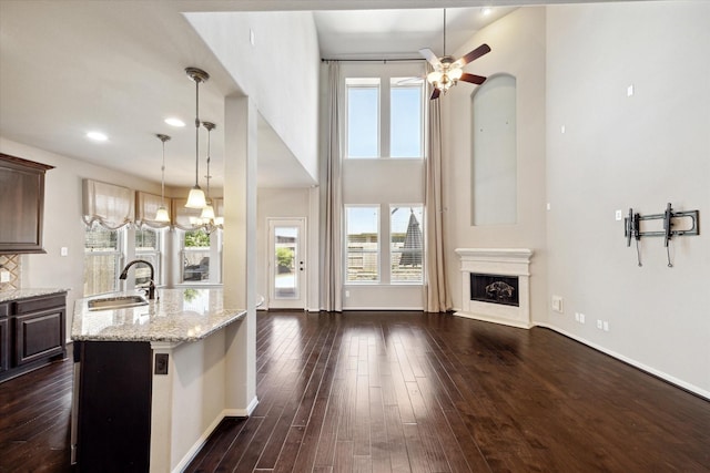 kitchen with dark wood-type flooring, a fireplace with raised hearth, ceiling fan with notable chandelier, a sink, and dark brown cabinetry