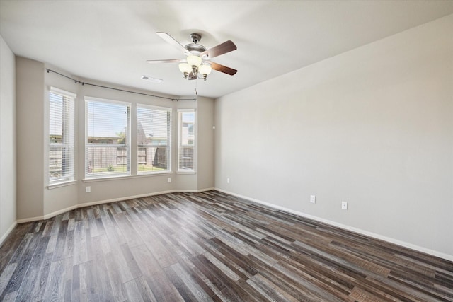 empty room featuring dark wood-type flooring, visible vents, baseboards, and a wealth of natural light