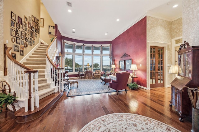 living area featuring hardwood / wood-style flooring, a towering ceiling, visible vents, and crown molding