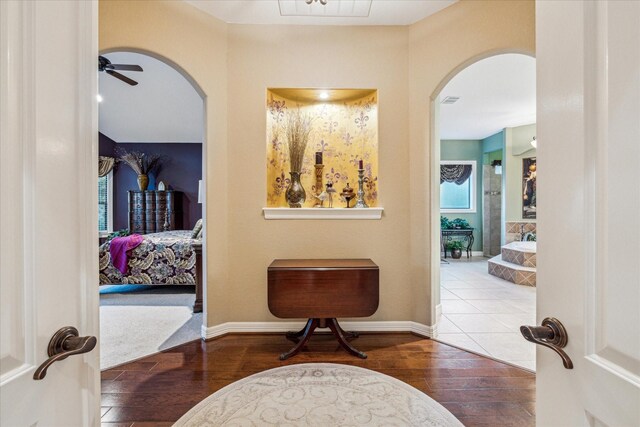 hallway featuring arched walkways, visible vents, hardwood / wood-style flooring, and baseboards