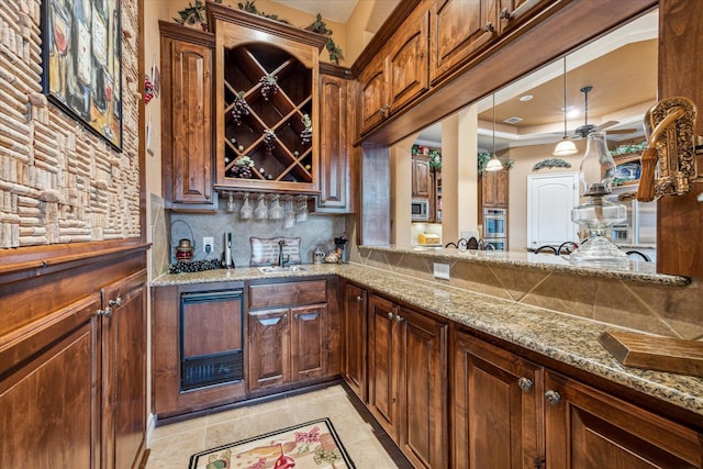 kitchen with light stone counters, stainless steel appliances, a sink, a tray ceiling, and tasteful backsplash