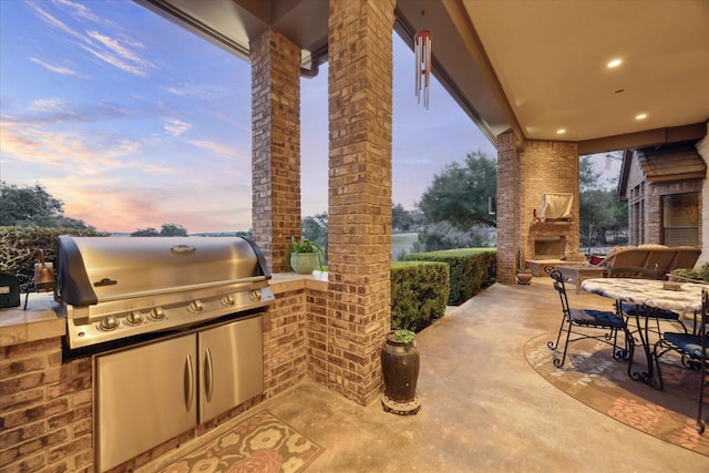 patio terrace at dusk with a grill, an outdoor kitchen, and an outdoor fireplace