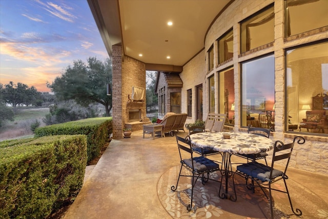 patio terrace at dusk featuring exterior fireplace and outdoor dining area