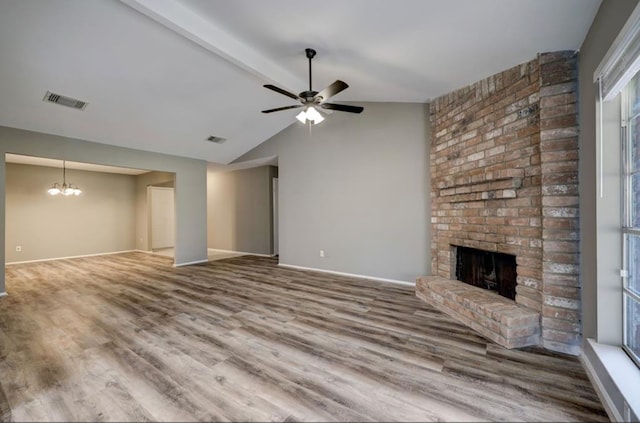 unfurnished living room with wood finished floors, baseboards, vaulted ceiling with beams, a brick fireplace, and ceiling fan with notable chandelier