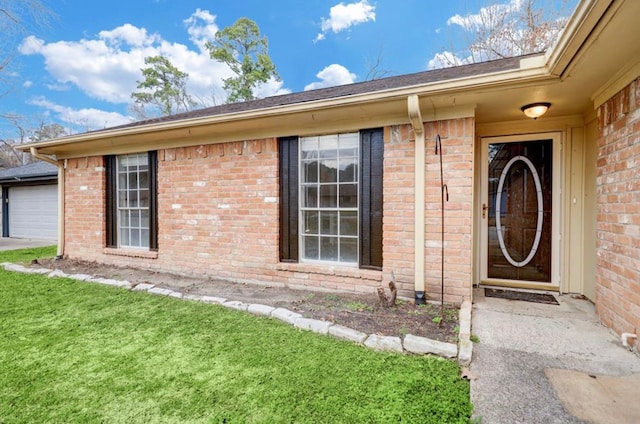 doorway to property with brick siding, a lawn, and a garage