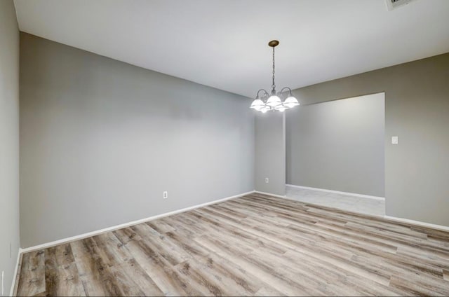 spare room with baseboards, a notable chandelier, and light wood finished floors