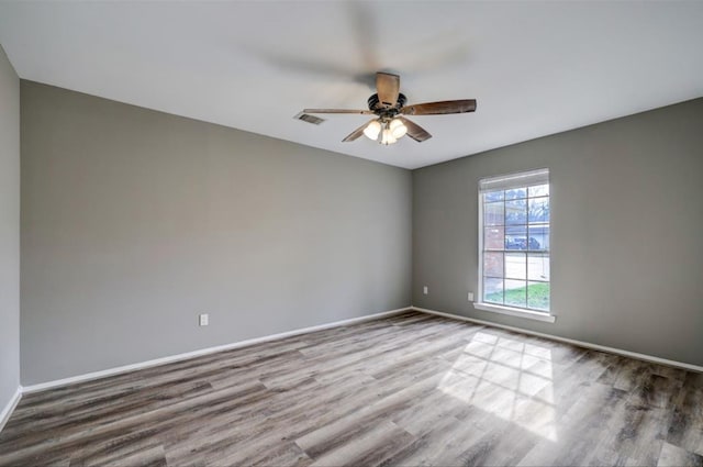 spare room featuring wood finished floors, a ceiling fan, visible vents, and baseboards