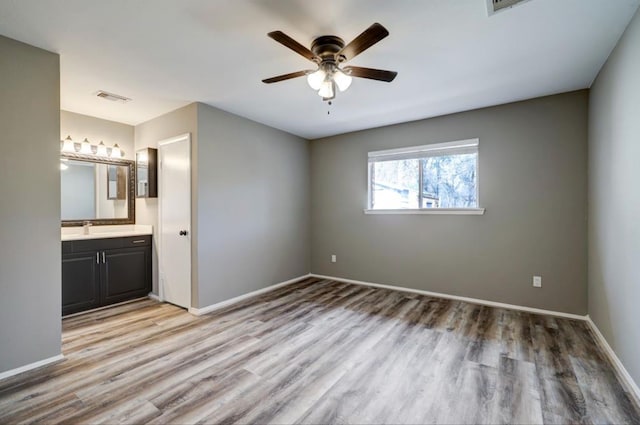 unfurnished bedroom with visible vents, a sink, ensuite bath, wood finished floors, and baseboards