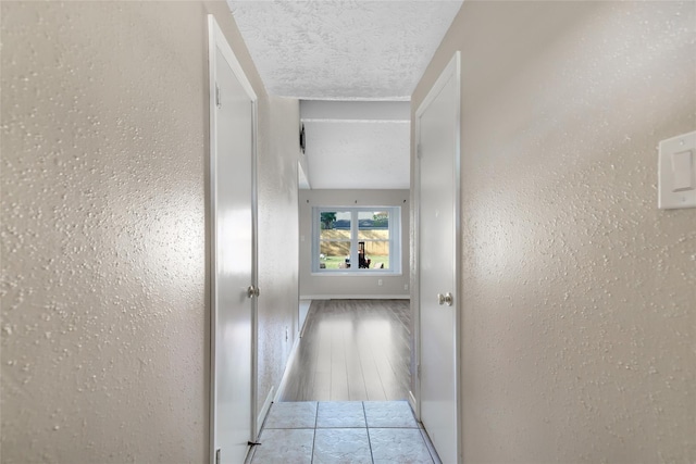 corridor featuring baseboards, a textured ceiling, and a textured wall