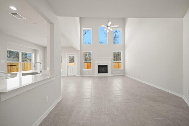unfurnished living room with baseboards, visible vents, a glass covered fireplace, ceiling fan, and a sink