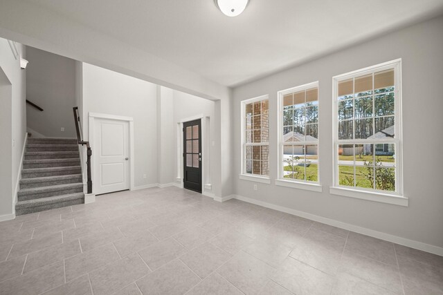 unfurnished living room with light tile patterned floors, baseboards, and stairway