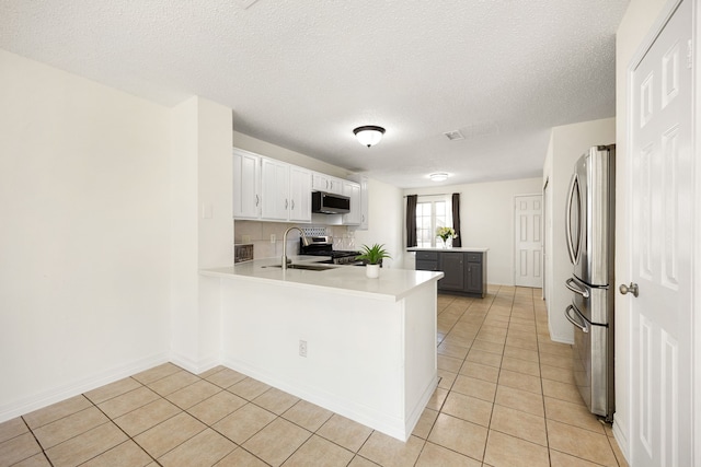 kitchen featuring light tile patterned floors, light countertops, appliances with stainless steel finishes, a sink, and a peninsula