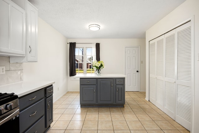 kitchen with light countertops, backsplash, gray cabinetry, light tile patterned flooring, and stainless steel gas range oven