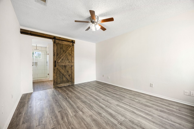 empty room featuring a textured ceiling, ceiling fan, a barn door, and wood finished floors