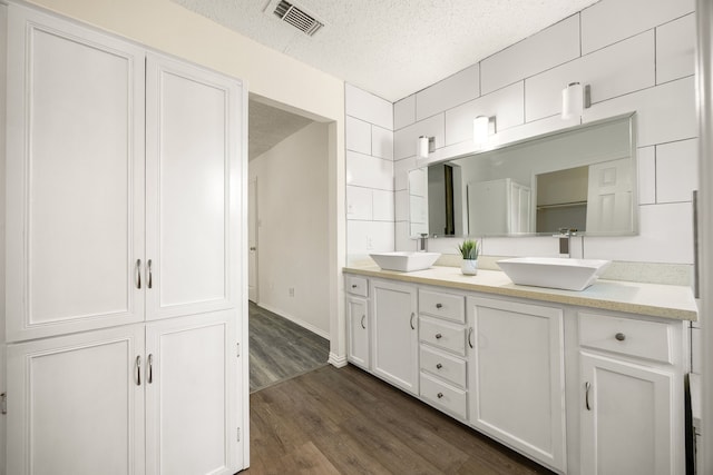 bathroom featuring a textured ceiling, double vanity, a sink, and visible vents