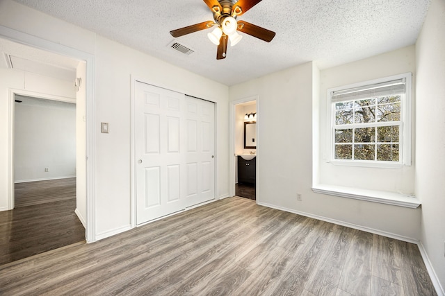 unfurnished bedroom with attic access, visible vents, wood finished floors, a textured ceiling, and a closet