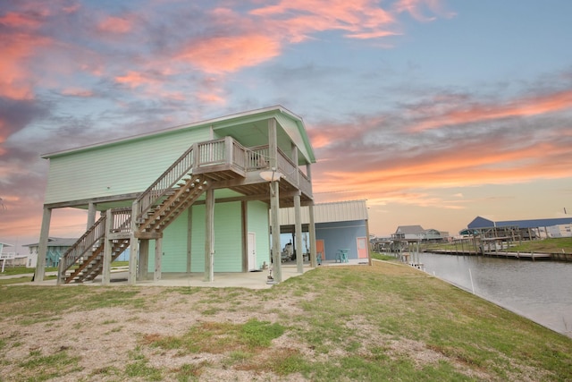 back of property at dusk with a yard, stairway, and a water view