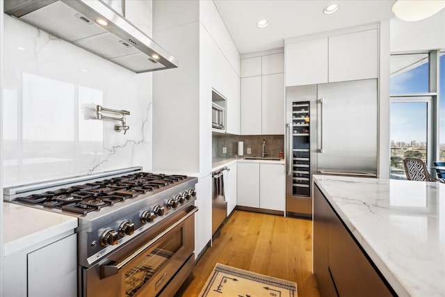 kitchen featuring premium appliances, a sink, white cabinets, wall chimney range hood, and decorative backsplash