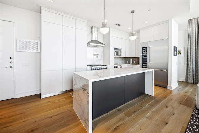 kitchen featuring light wood-style flooring, white cabinets, wall chimney range hood, appliances with stainless steel finishes, and modern cabinets