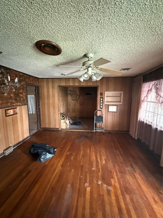 unfurnished living room featuring a textured ceiling, ceiling fan, wood walls, wood finished floors, and visible vents