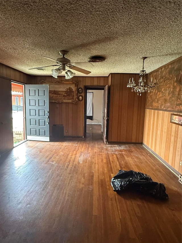 interior space featuring wooden walls, a textured ceiling, hardwood / wood-style floors, and ceiling fan with notable chandelier