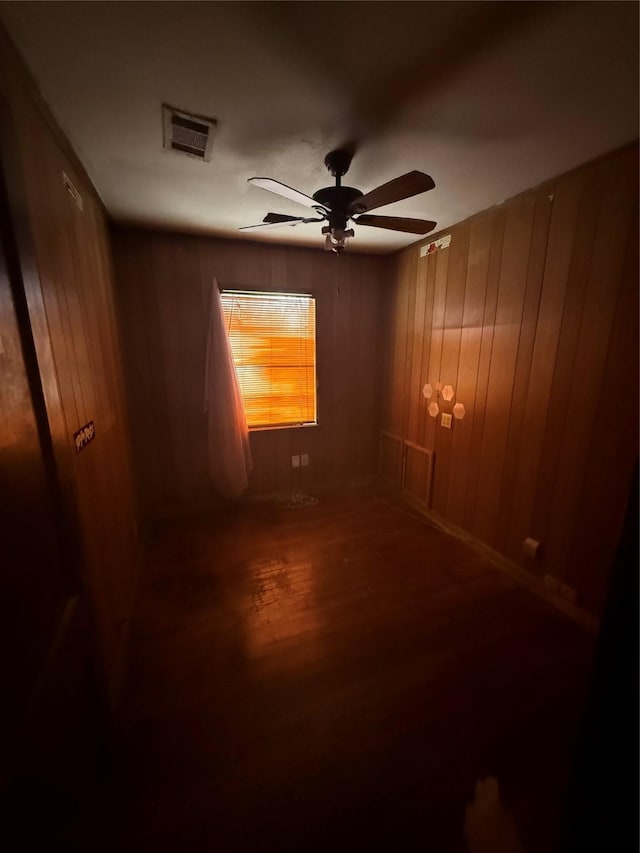 unfurnished room with a ceiling fan, visible vents, wooden walls, and wood finished floors