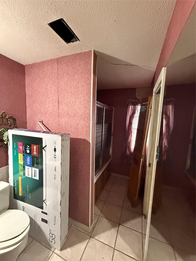 bathroom with toilet, a textured ceiling, and tile patterned floors