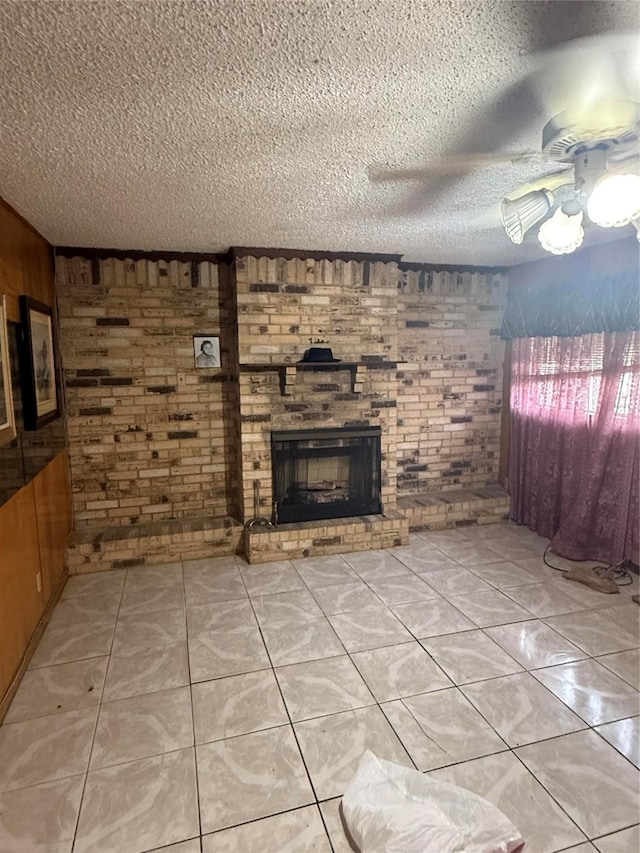 unfurnished living room featuring a fireplace, light tile patterned floors, wooden walls, a textured ceiling, and brick wall