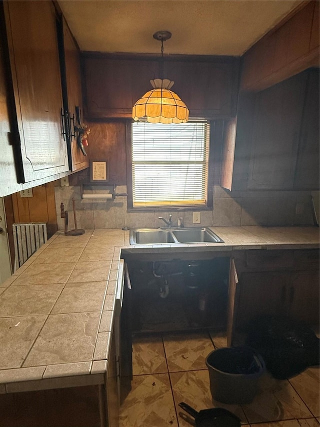 kitchen with a sink, tile counters, and decorative light fixtures