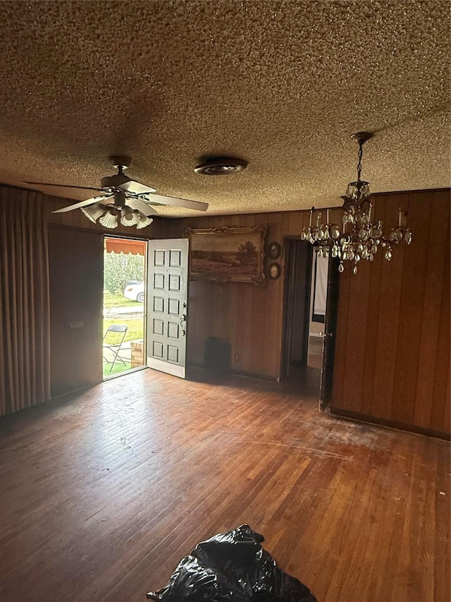 unfurnished living room featuring hardwood / wood-style flooring, wooden walls, a textured ceiling, and ceiling fan with notable chandelier