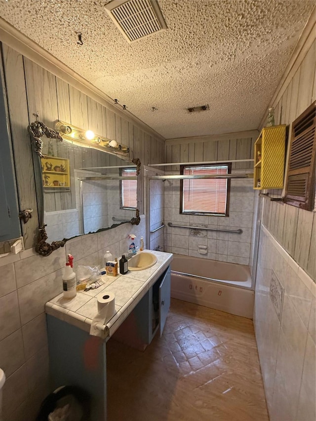 full bath featuring a textured ceiling, visible vents, bath / shower combo with glass door, and tile walls