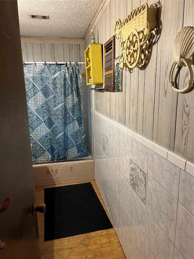 bathroom featuring visible vents, wainscoting, shower / bath combination with curtain, a textured ceiling, and tile walls