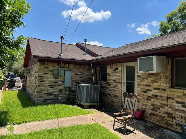 rear view of house with a shingled roof, cooling unit, and a lawn