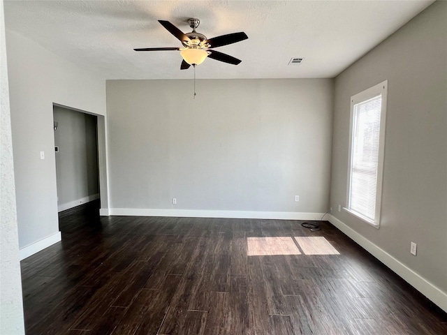 spare room with dark wood-type flooring, a ceiling fan, visible vents, and baseboards