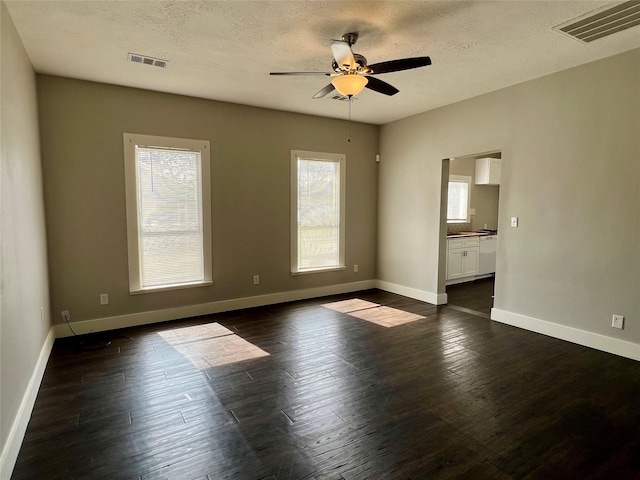 spare room with a textured ceiling, dark wood-style flooring, visible vents, and baseboards