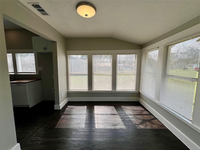 interior space with dark wood-style flooring, visible vents, vaulted ceiling, a textured ceiling, and baseboards