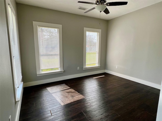 empty room with dark wood-style floors, plenty of natural light, visible vents, and baseboards