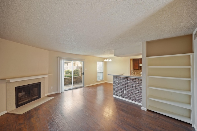 unfurnished living room featuring a textured ceiling, a tile fireplace, wood finished floors, baseboards, and an inviting chandelier