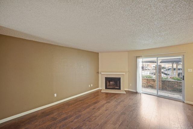 unfurnished living room featuring a fireplace with flush hearth, baseboards, dark wood finished floors, and a textured ceiling