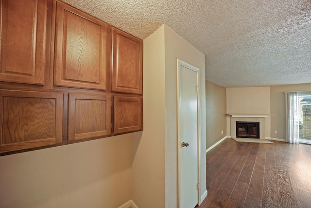 interior space featuring a textured ceiling, wood-type flooring, a fireplace with flush hearth, and baseboards