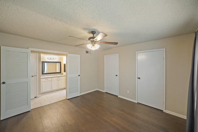 unfurnished bedroom with a textured ceiling, baseboards, dark wood-type flooring, and ensuite bathroom