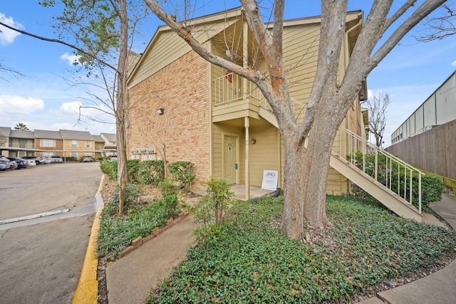 view of home's exterior with uncovered parking, brick siding, and stairs