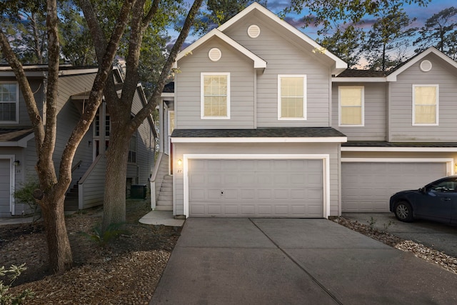 townhome / multi-family property featuring driveway, a shingled roof, a garage, and central AC unit