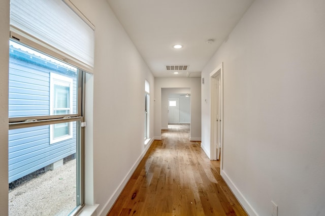 corridor with a wealth of natural light, wood finished floors, visible vents, and baseboards